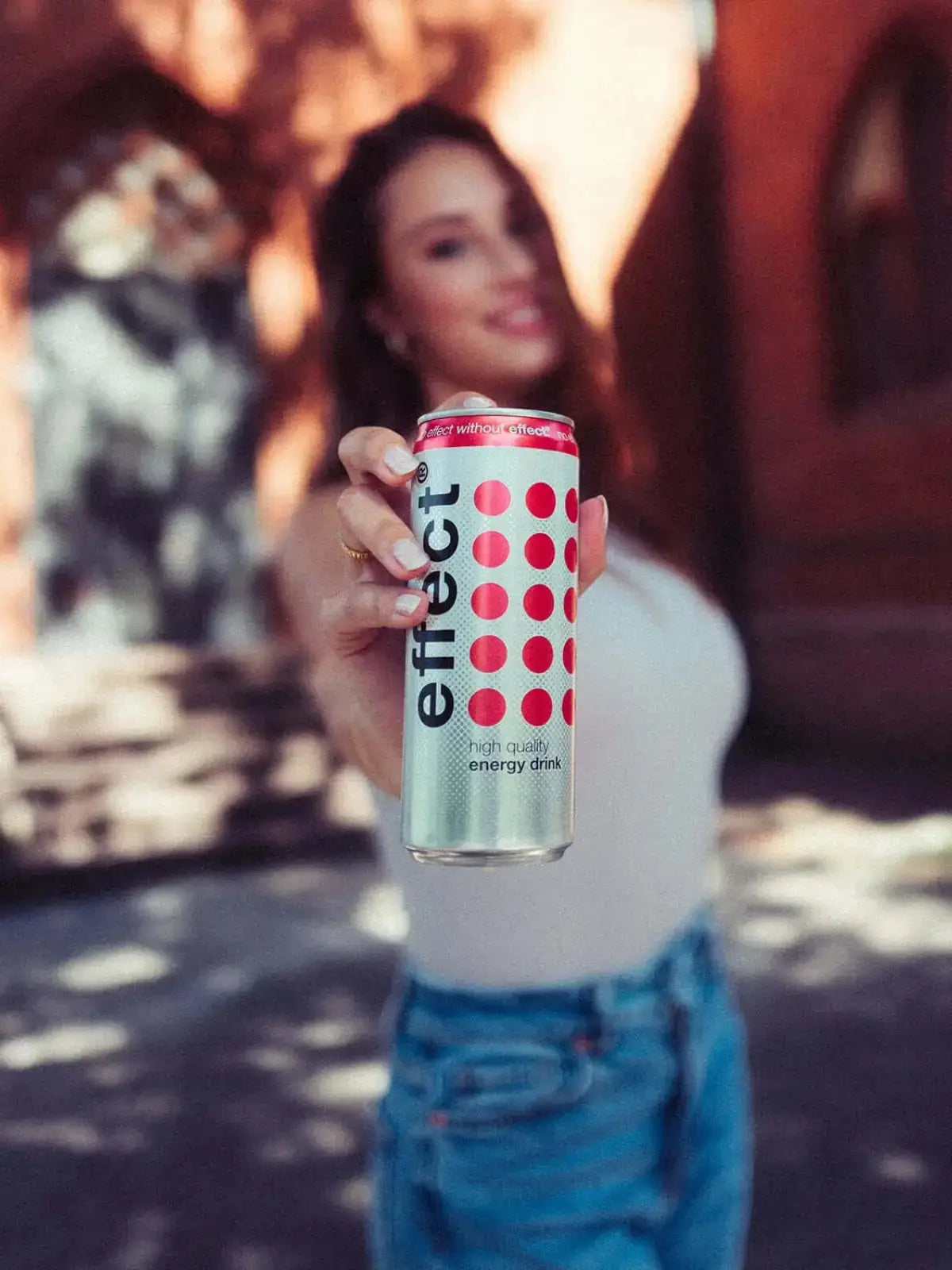Eine Frau steht draußen und hält eine Dose effect Classic Energydrink in der Hand