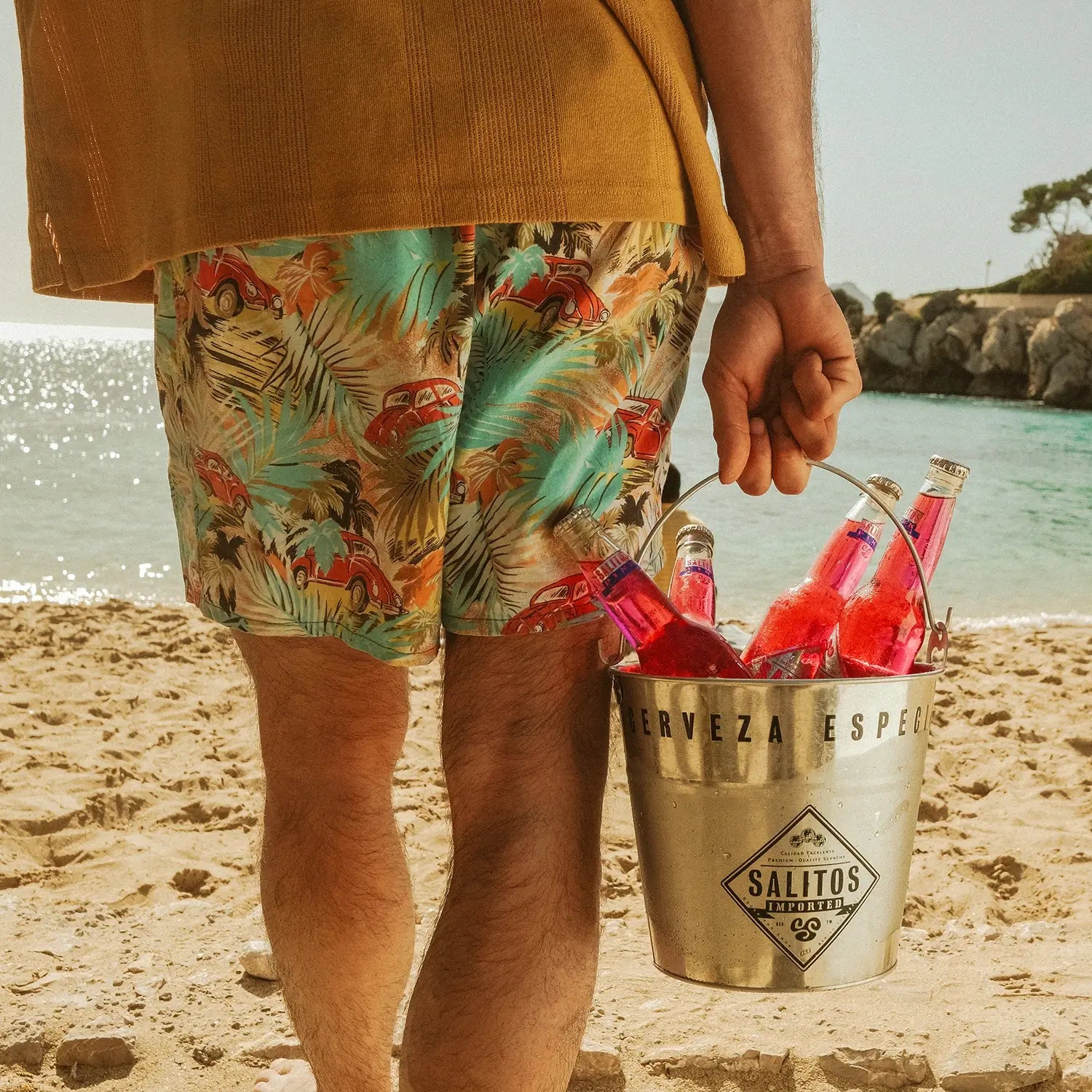 Ein Mann geht am Strand zum Wasser. In der rechten Hand hält er einen silbernen Eimer mit SALITOS Schriftzug. In diesem Eimer befinden sich 4 Flaschen von SALITOS Pink