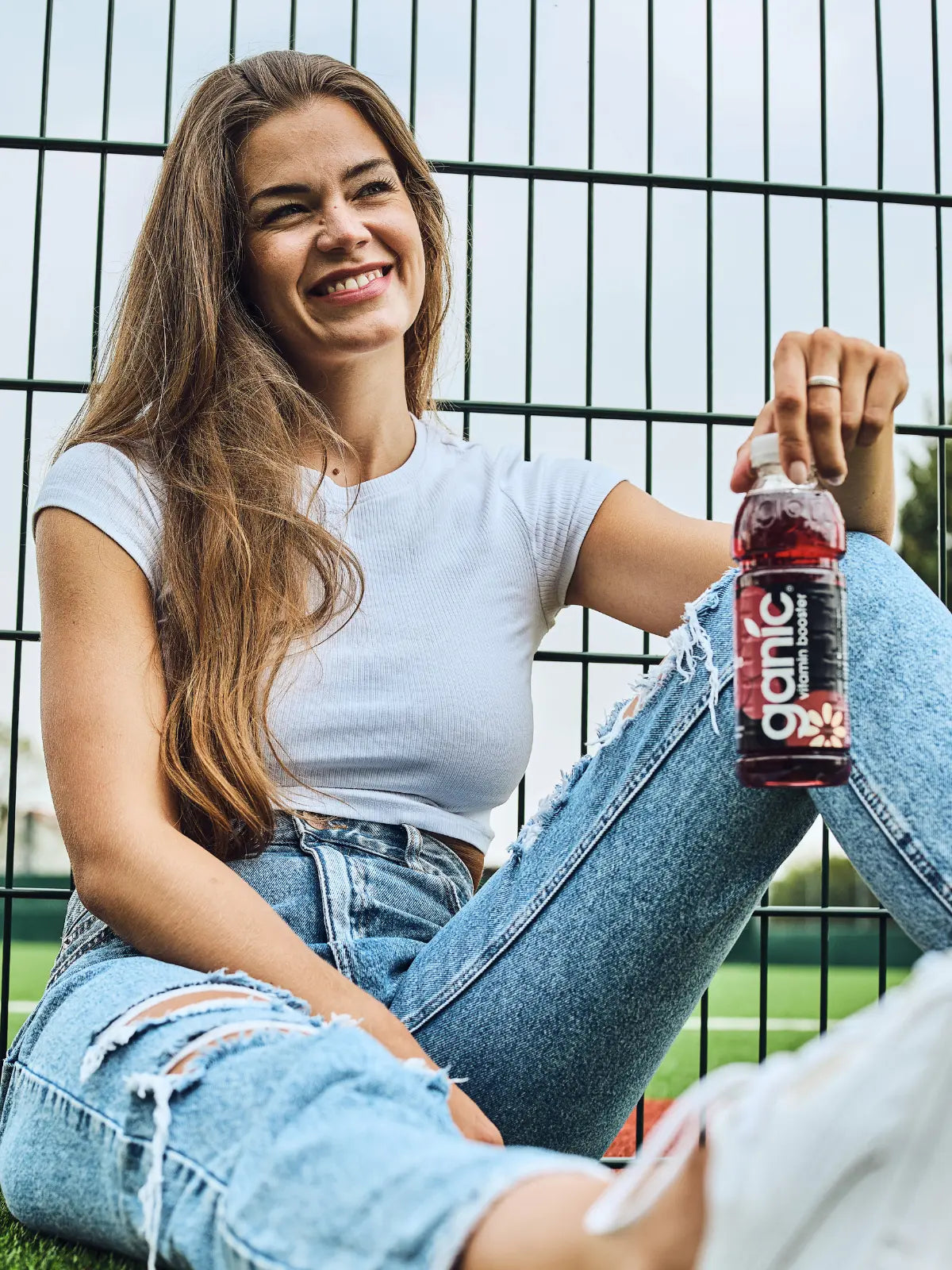 eine frau sitzt an einem zaun und hält eine flasche ganic traube acai