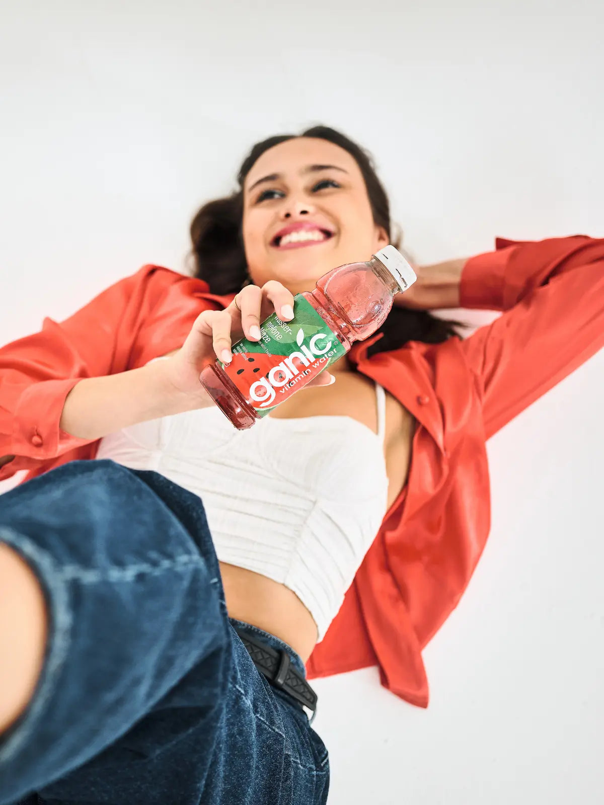 eine glückliche frau liegt auf dem boden und hält eine flasche ganic wassermelone minze