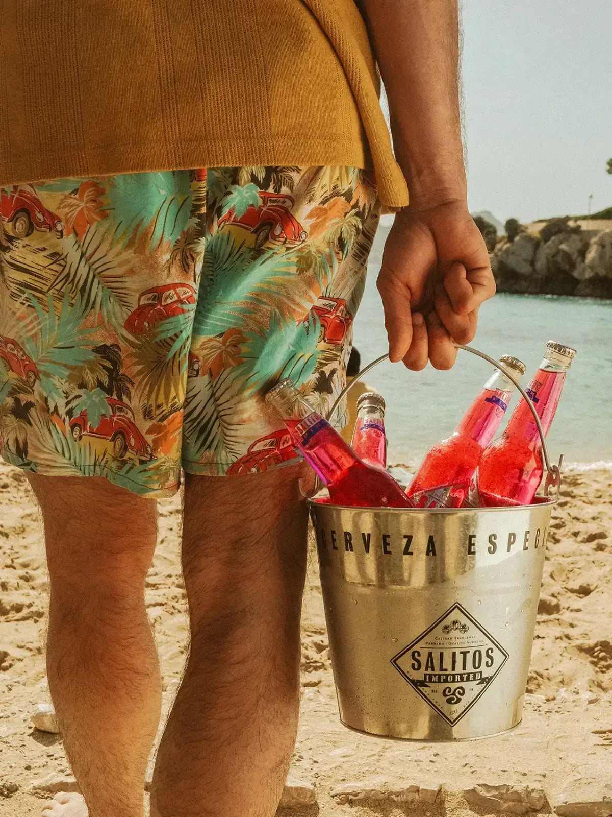 Ein Mann hält einen silbernen Eimer mit SALITOS Pink Flachen am Strand.