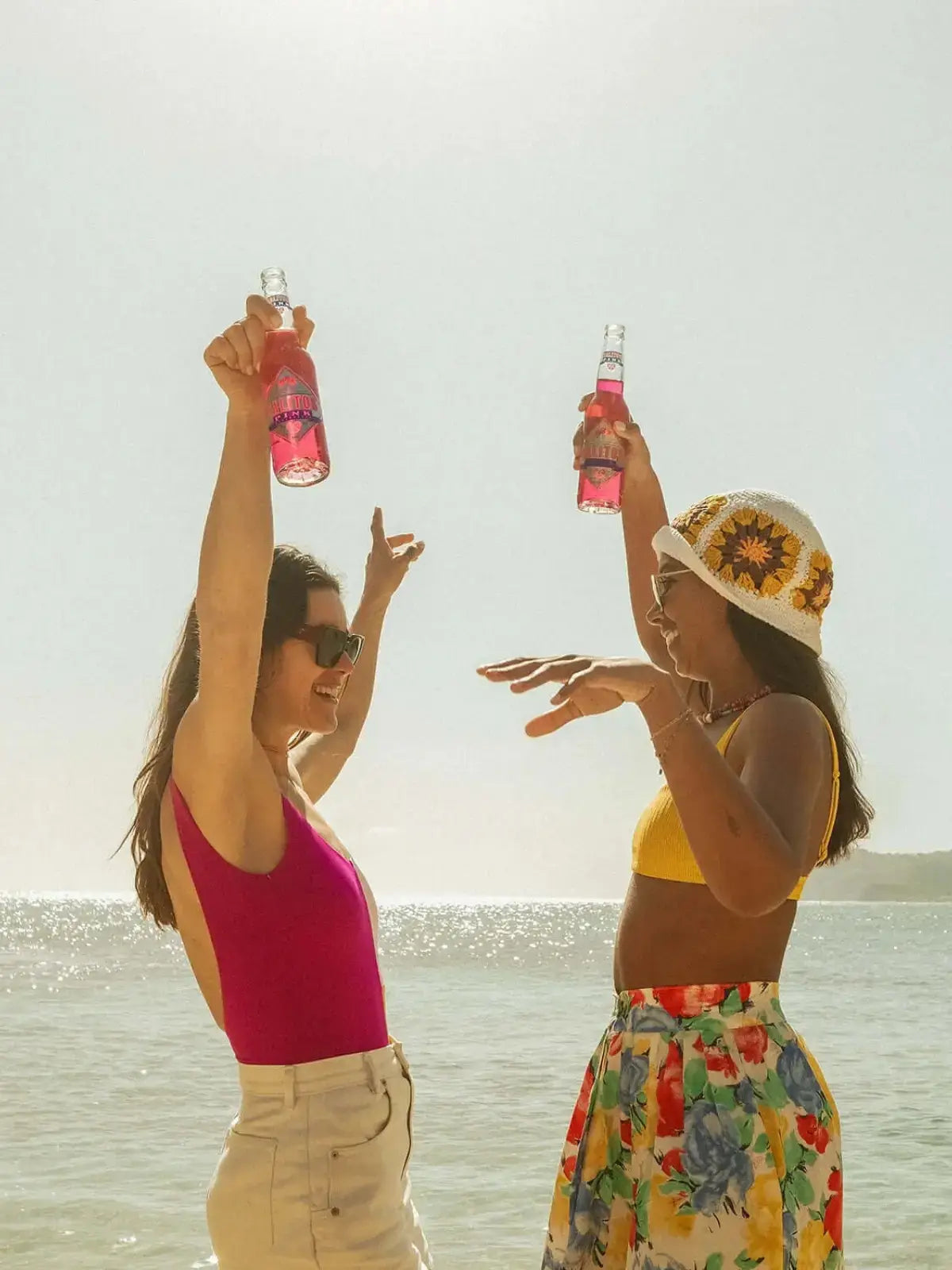 2 Frauen die am Strand tanzen und deibei SALITOS Pink in der Händen halten