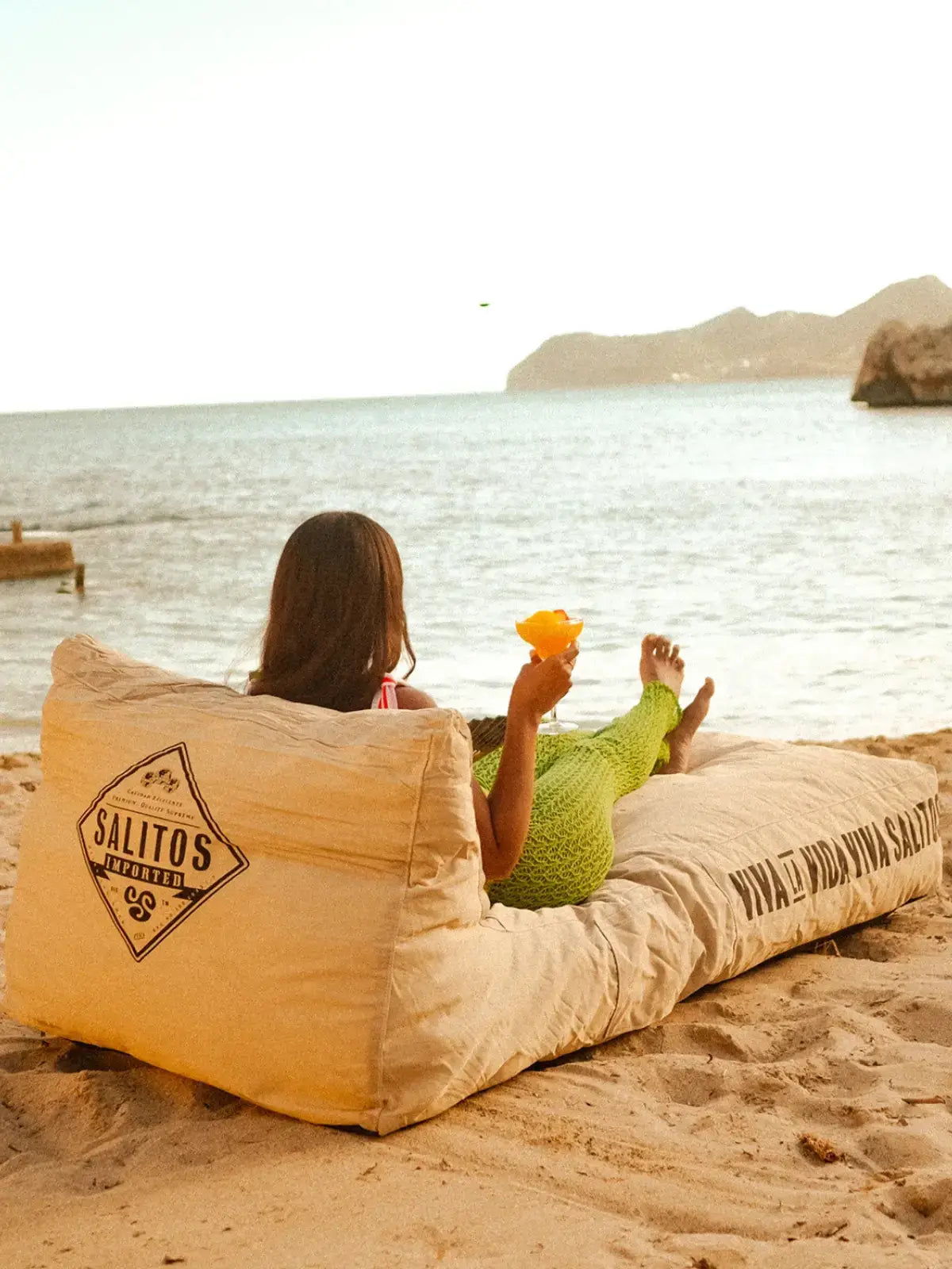 Am Strand sitzt eine Frau auf einem Sitzsack und relaxt, umgeben von Sand und Wellen.