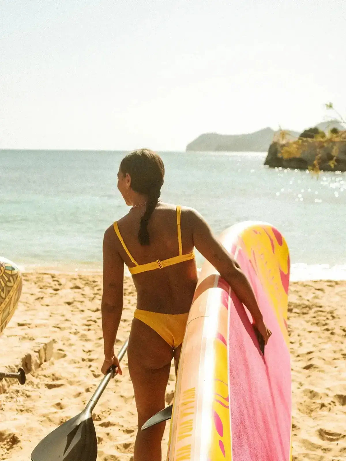 Eine Frau die am Strand zum Meer geht und dabei das SALITOS Stand up Board trägt.