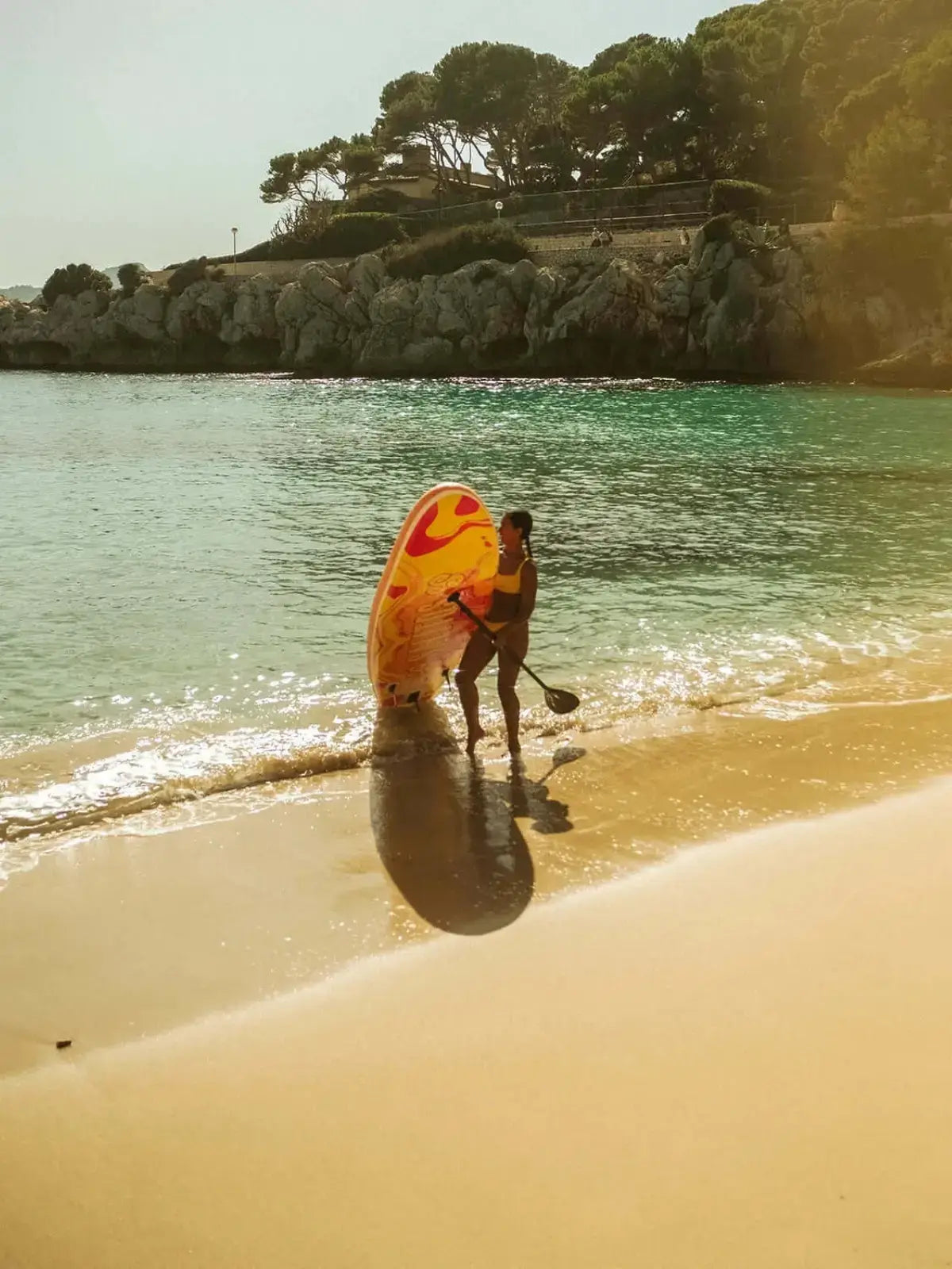 Eine Frau die am Strand im Wasser steht und das STAND up Board von SALITOS in der Hand hält