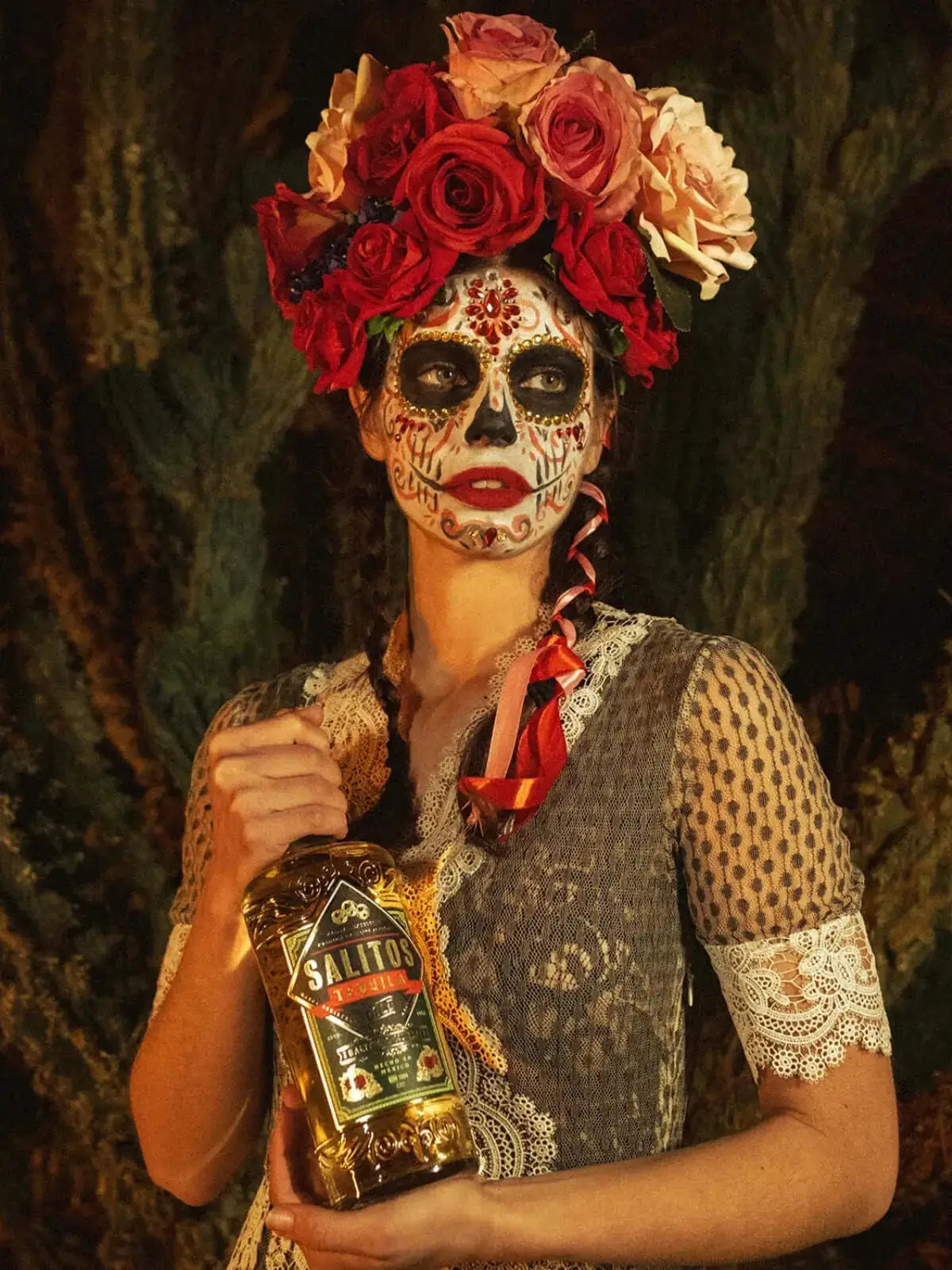 Eine Frau geschminkt wie ein Totenkopf hat eine Krone aus Blumen und in der Hand hält Sie eine Flasche SALITOS Tequila Gold