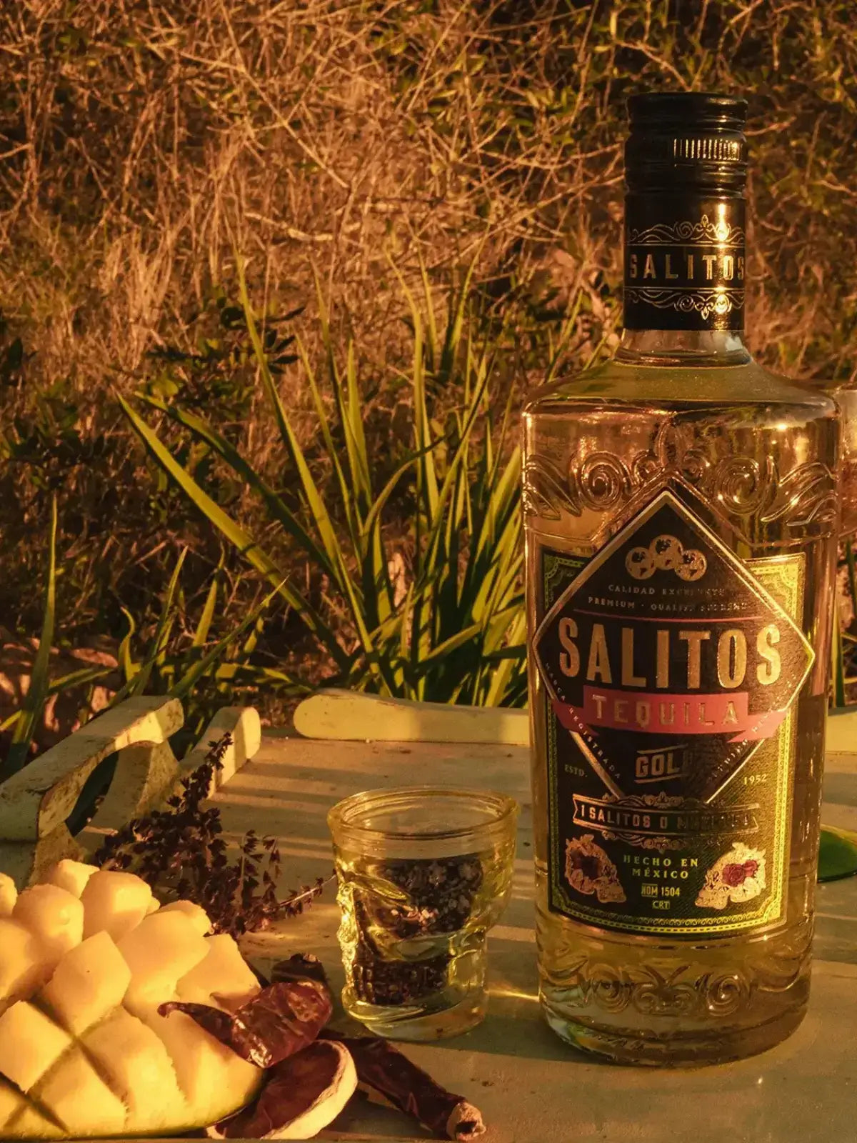 Eine Flasche SALITOS Tequila Gold umgeben von tropischen Früchten.