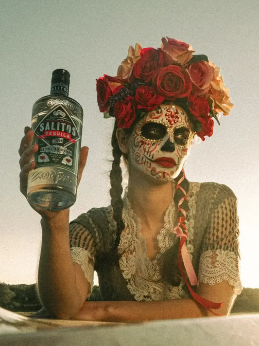 Eine Frau geschminkt wie ein Totenkopf hat eine Krone aus Blumen und in der Hand hält Sie eine Flasche SALITOS Tequila Silver